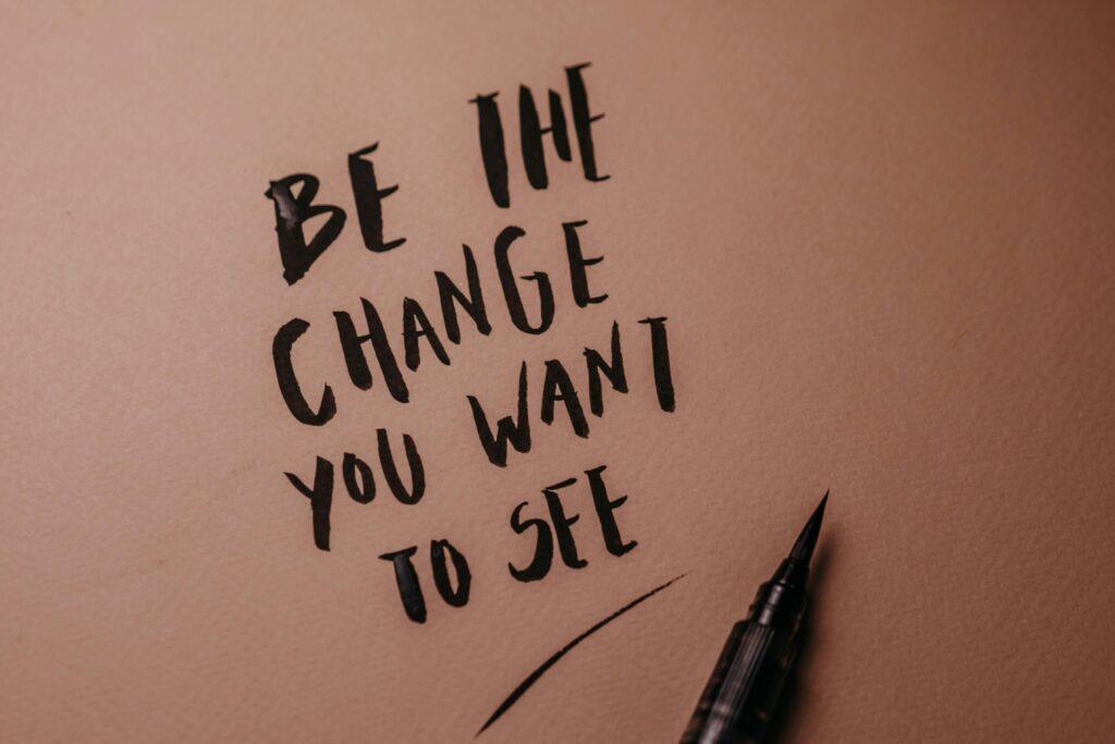Motivational calligraphy reads 'Be the change you want to see' on a pink surface.